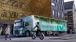 An illustration of Unilever’s first electric truck driving through a town in the Netherlands. Text on the side reads: Fully charged. Zero emissions. This truck is 100% electric.